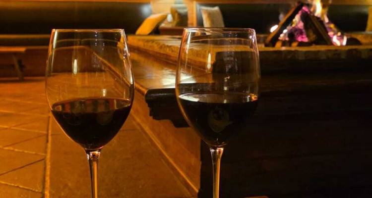 Twee glazen rode wijn op een houten tafel naast een gloeiende open haard.