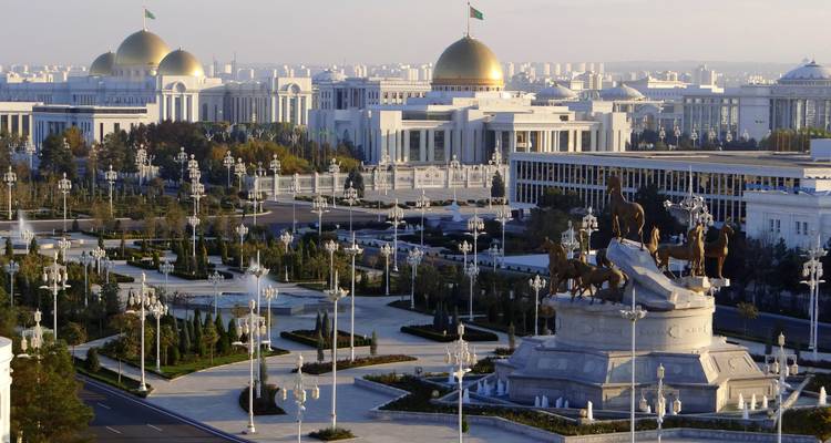 Vue panoramique des bâtiments gouvernementaux en marbre blanc d'Achgabat avec des toits à coupoles dorées entourés de jardins entretenus.