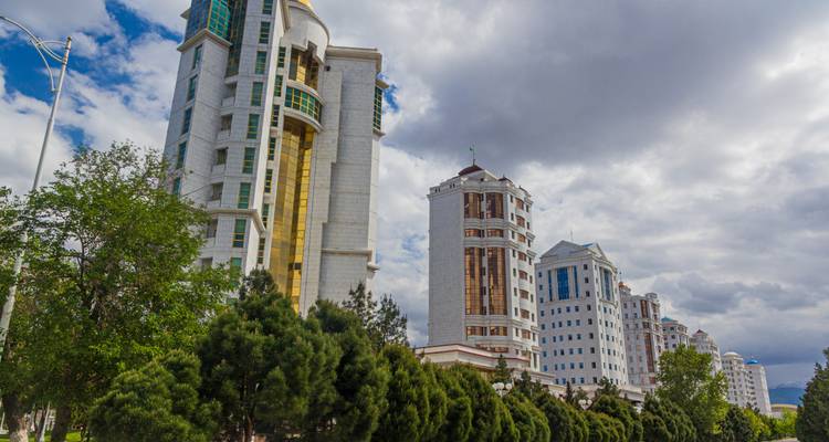 Des gratte-ciel modernes en marbre et verre bordant un boulevard arboré à Achgabat sous un ciel dramatique.