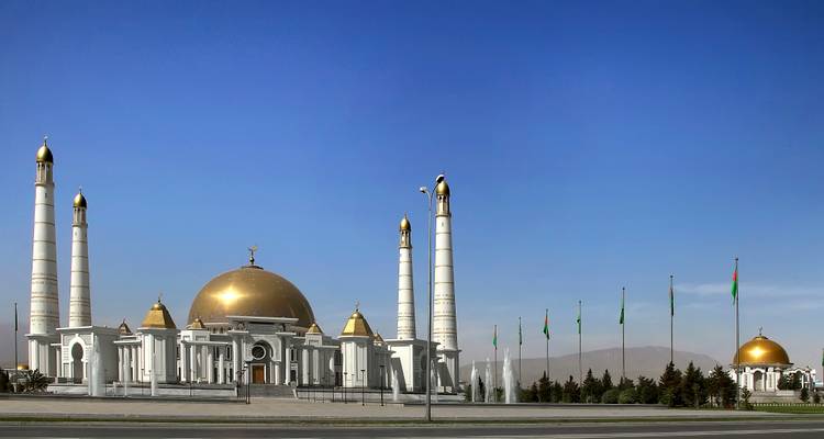Monument de l'Indépendance du Turkménistan en marbre blanc et or avec des minarets contre un ciel bleu dégagé.