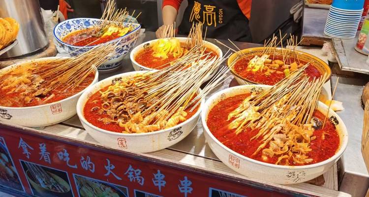 Bowls of spicy red hotpot broth filled with skewered street snacks at a food stall