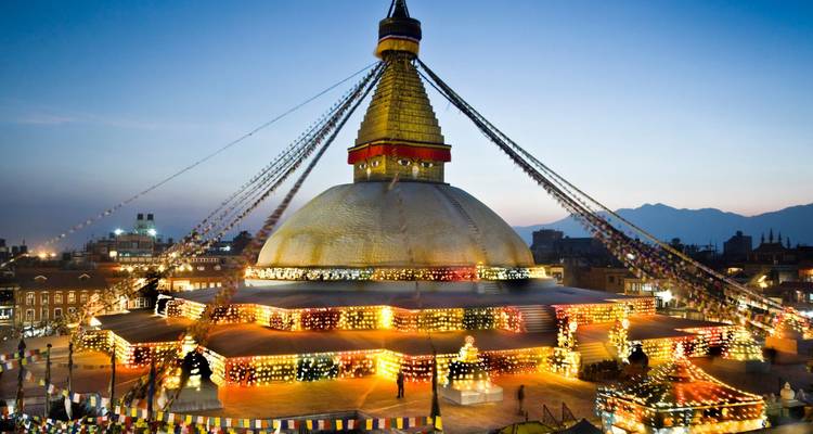 Abendbeleuchtung der massiven Boudhanath-Stupa in Kathmandu mit Gebetsfahnen, die sich zum Dämmerhimmel erstrecken.