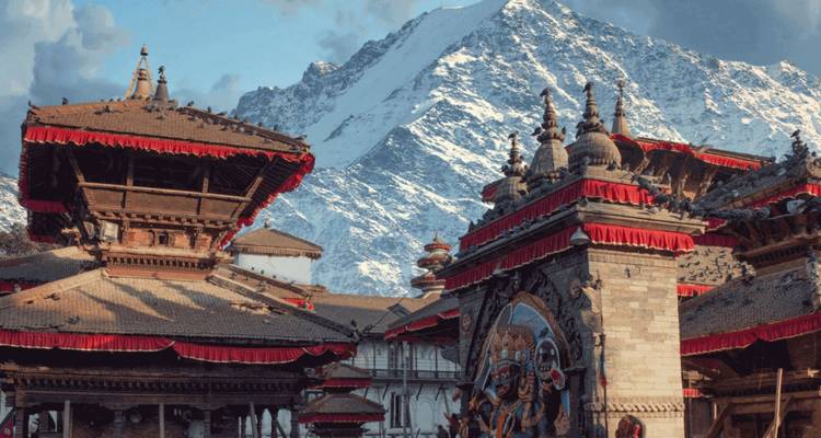 Traditionelle nepalesische Tempeldächer mit leuchtend roten Verzierungen vor einem aufragenden schneebedeckten Berg