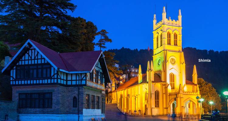 Night view of the illuminated Christ Church and adjoining timber-framed building in Shimla against a deep blue sky.