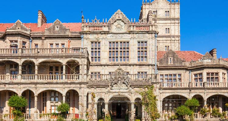 Historic Viceregal Lodge in Shimla featuring grey stone architecture against a vivid blue sky.