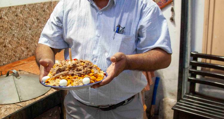 Homme tenant un plateau de plov traditionnel garni d'œufs de caille et de viande.
