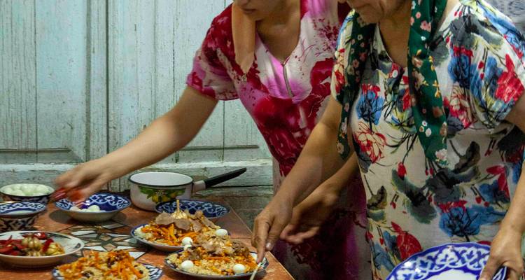 Femmes disposant plusieurs assiettes de plov et de salades sur une table en bois rustique.