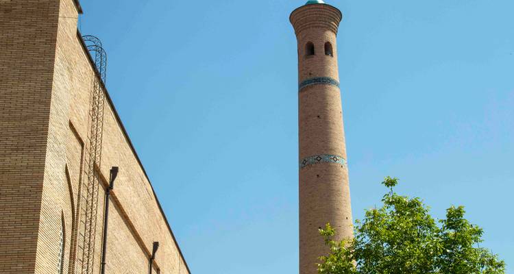 Grand minaret en brique avec des bandes à motifs bleus s'élevant vers un ciel bleu dégagé.