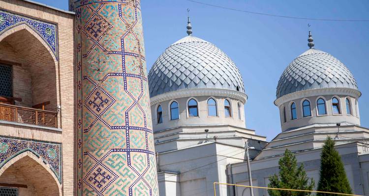 Minaret à motifs et deux dômes gris argenté d'une mosquée vus de côté.