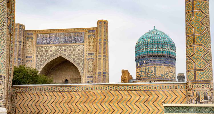 Vue partielle du complexe du Registan montrant des murs carrelés et un dôme turquoise par temps couvert.