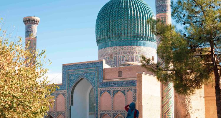 Voyageur photographiant le complexe Gur-e Amir encadré par des arbres sous un ciel dégagé.