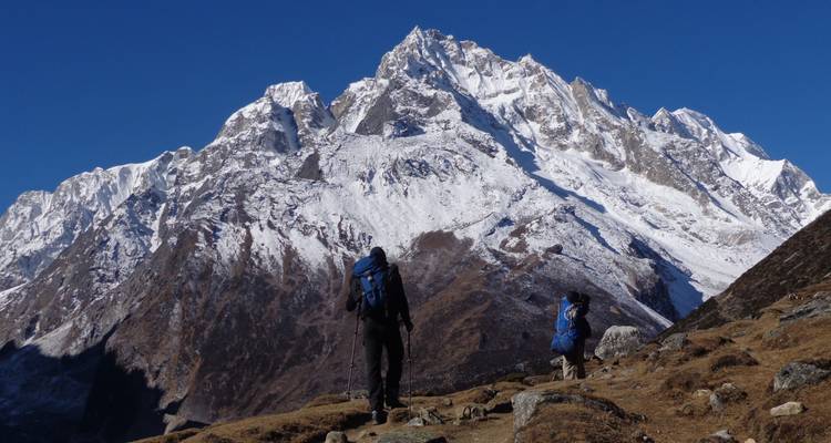 Trekkers gaze at towering snow-covered Annapurna peaks under a crisp blue sky.