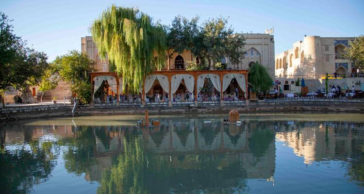 Restaurant au bord de l'eau avec des auvents drapés se reflétant dans l'étang tranquille de Lyabi Hauz.