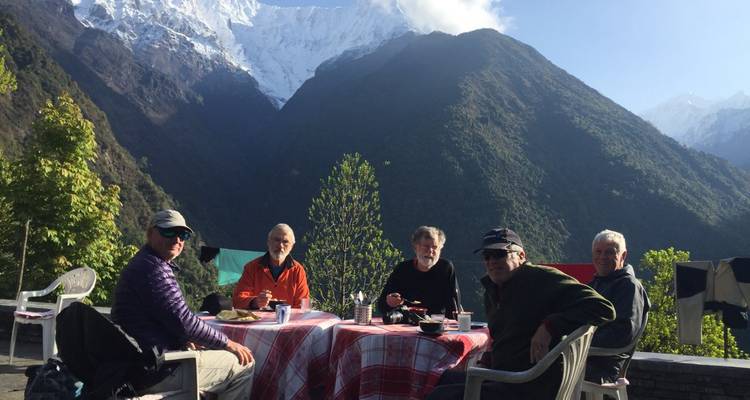 Group of trekkers enjoy breakfast outdoors with towering Himalayan peaks behind.
