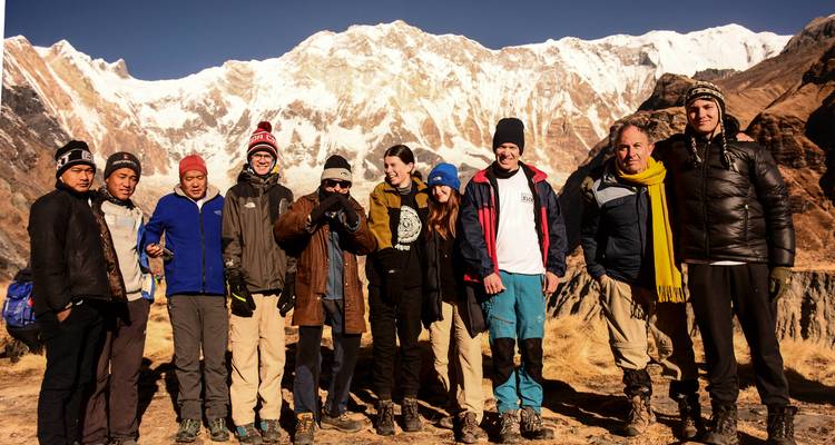 Large trekking group poses in front of the snowy amphitheatre of Annapurna Base Camp.