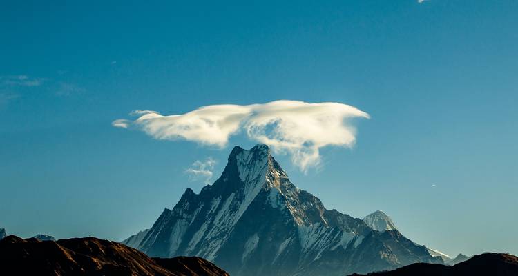 Distinctive Machhapuchhre peak with a lenticular cloud cap against a clear blue sky.