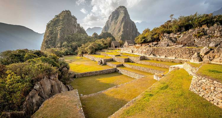 Ruinas de piedra escalonadas de Machu Picchu respaldadas por dramáticos picos verdes bajo la suave luz del sol.