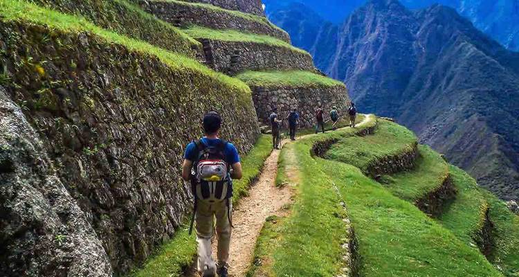 Mochileros caminando por un sendero serpenteante de piedra a lo largo de terrazas verdes empinadas en lo alto de los Andes.