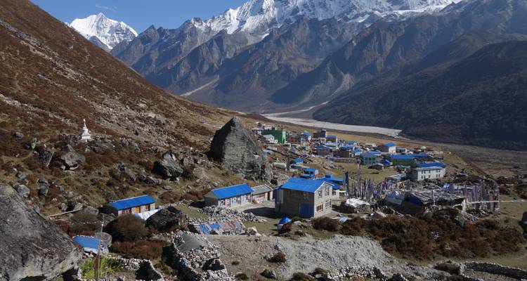 Remote mountain village with blue-roofed houses nestled in a broad valley beneath snowy Himalayan peaks.