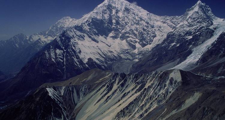 High, rugged snow-clad Himalayan massif rising above steep glacial valleys under deep blue sky.