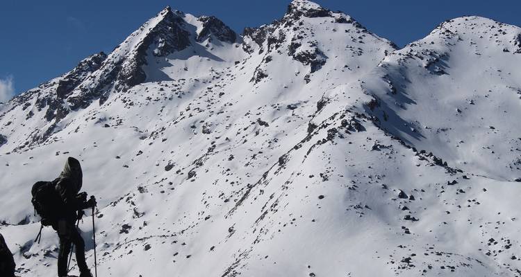Mountaineer with backpack pauses on a snowy ridge overlooking rugged alpine peaks.