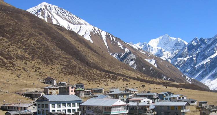 Small Himalayan village beneath snow-covered peaks on a clear day (similar to previous).