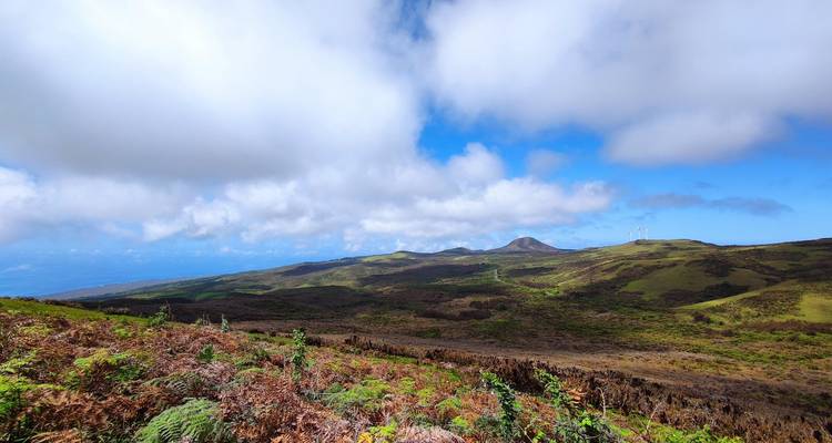 Wide highland vista of rolling volcanic hills under scattered clouds and bright blue sky.