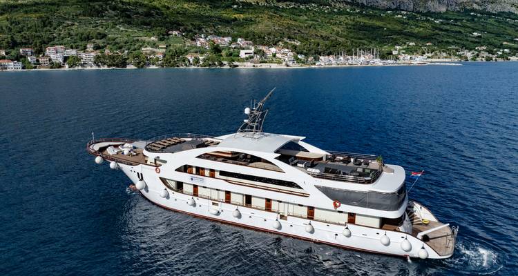 Aerial view of a sleek white yacht cruising on deep-blue Adriatic waters with coastline in the background.