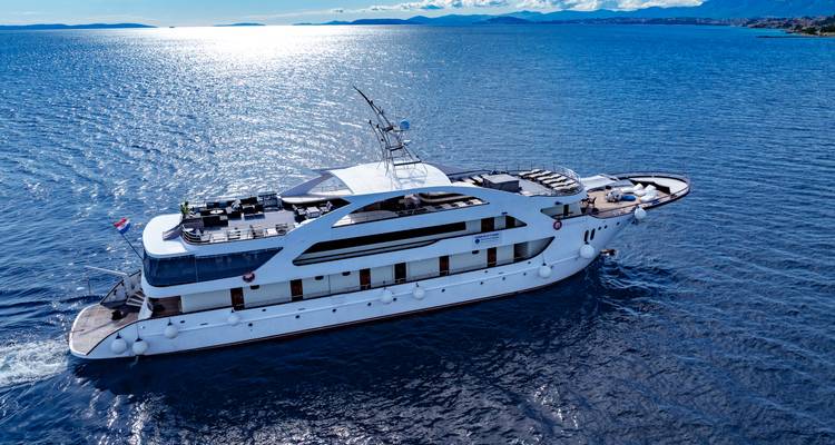 Drone shot of luxury yacht gliding across shimmering blue sea at midday.