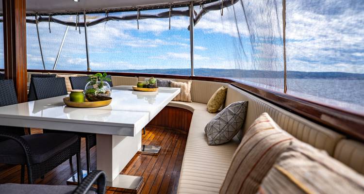 Covered outdoor dining table with cushioned seating on a yacht overlooking the water.