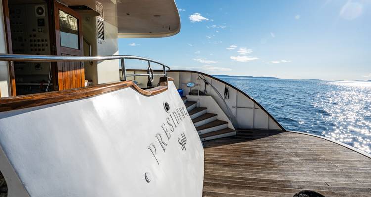 Stern platform of yacht showing name plate and steps down to the water on a sunny day.