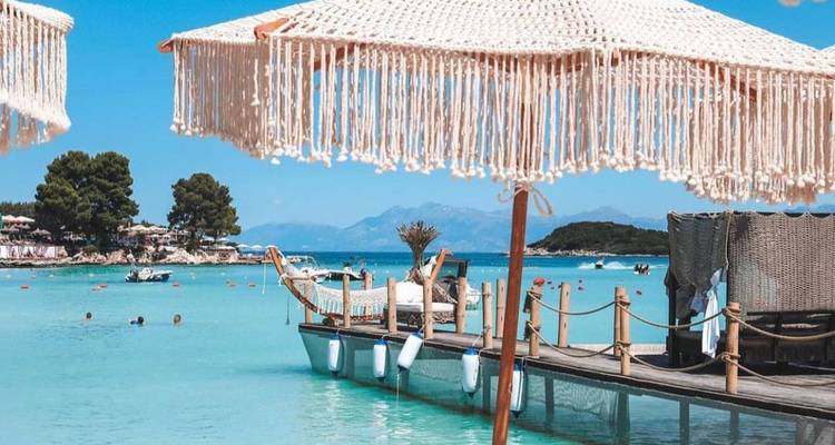 Turkooizen lagune met gefranjede parasols en houten pier bij de idyllische stranden van Ksamil.