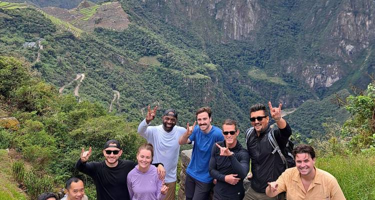 Groupe de randonneurs heureux posant sur un sentier de montagne luxuriant surplombant la route sinueuse et les vallées verdoyantes près du Machu Picchu.