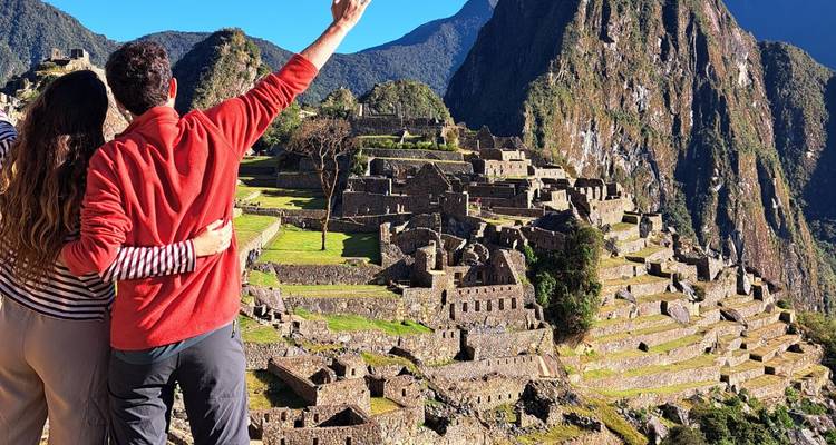 Couple s'embrassant en contemplant les terrasses de pierre emblématiques et les sommets du Machu Picchu par une journée claire.