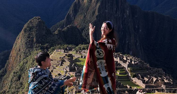 Deux voyageurs en ponchos colorés se saluant avec les ruines spectaculaires du Machu Picchu derrière eux.