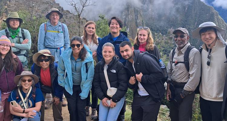Randonneurs souriants rassemblés sur un point de vue du sentier avec les pics enveloppés de nuages du Machu Picchu en arrière-plan.