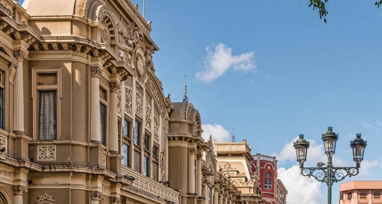 Historisch neoklassiek gebouw met sierlijke gevel en vintage lantaarnpalen in het centrum van San José onder een blauwe hemel.