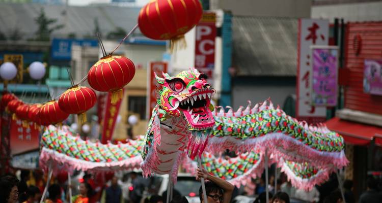 Levendige straatoptocht met een kleurrijke draakpop en rode lantaarns tijdens een Chinees festival.