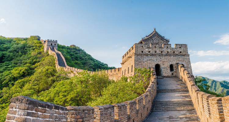 Iconic Great Wall of China snaking over lush green hills under blue sky.