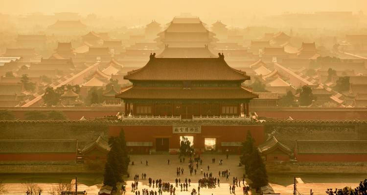 Misty golden sunrise view over Forbidden City rooftops with visitors below.