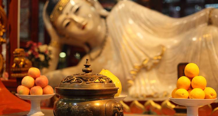Primer plano de una estatua de Buda de jade reclinado con ofrendas de fruta en primer término.