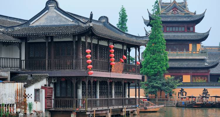 Casas tradicionales de madera de pueblo acuático con faroles rojos junto a un canal tranquilo.