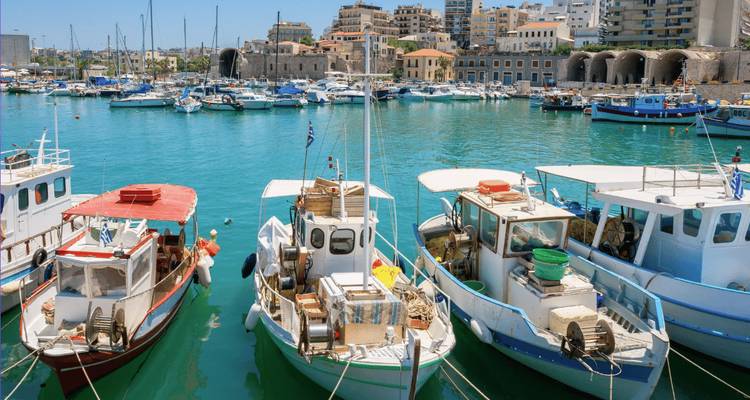 Los coloridos barcos de pesca se mecen en el puerto histórico de Heraklion con los edificios de la ciudad al fondo.