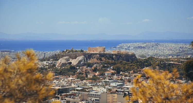Verre telefoto zicht op de Acropolis die boven Athene uittorent met de blauwe Egeïsche Zee op de achtergrond.