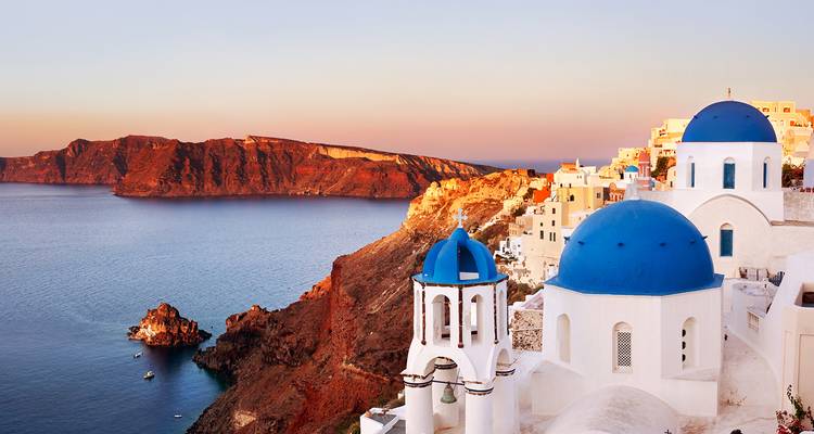 Iconic blue-domed churches of Oia overlook the caldera cliffs of Santorini at golden sunset.