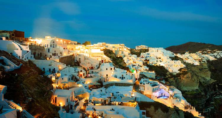 Nightfall panorama of Oia with whitewashed houses cascading down cliffs illuminated by warm lights.