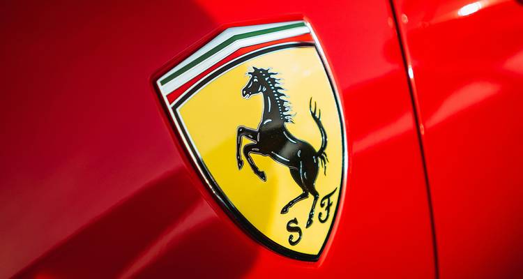 Primer plano del emblema de Ferrari del caballo amarillo encabritado en un auto rojo brillante.