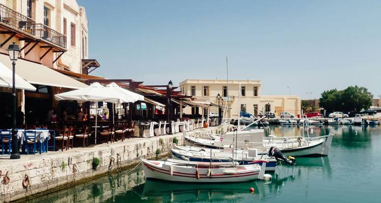 Encantador puerto veneciano bordeado de cafés, sombrillas y pequeños botes de pesca en aguas tranquilas color turquesa.