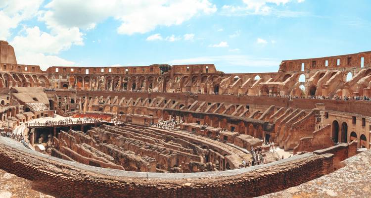 Intérieur panoramique du Colisée de Rome avec des gradins en pierre étagés et des visiteurs explorant le sol de l'arène.