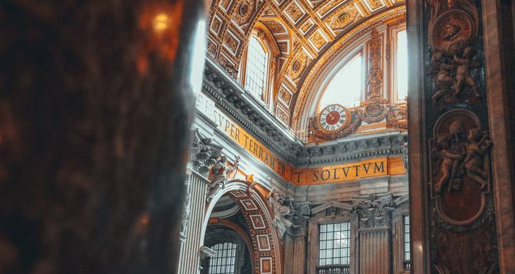 Intérieur détaillé de la basilique Saint-Pierre avec plafond doré orné, colonnes et inscriptions latines éclairés par une lumière douce.